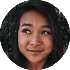 Image of a young Asian girl facing the camera with her eyes looking to the left against a foliage backdrop