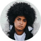 Image of young black woman with a large afro looking at the camera with a white shirt and black coat